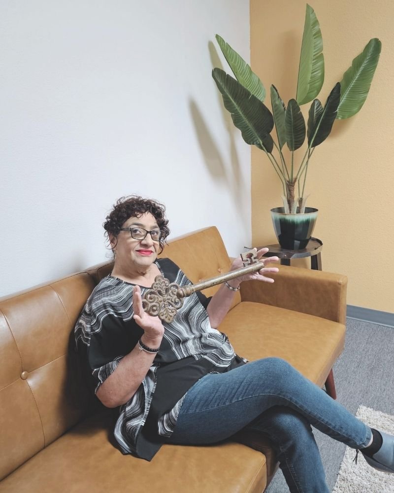 Sally Scheidemantle sitting on a sofa holding a large golden key, representing luxury real estate success at Crown Realty Services.